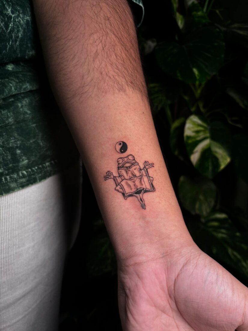 Fine line frog with yin-yang wrist tattoo by The Quinted